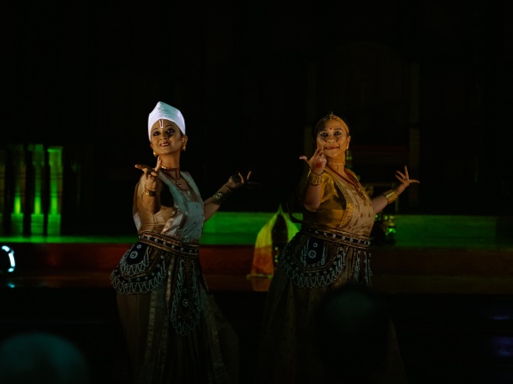 Two women in Southeast Asian cultural garb perform a dance with hand movements